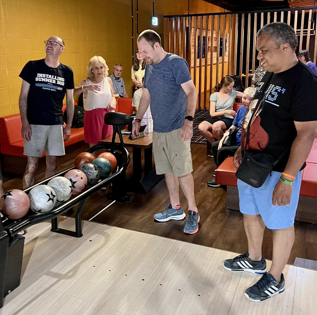 People gather around a set of balls in a bowling alley.