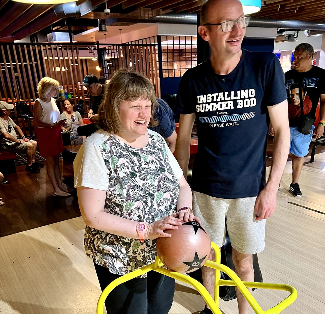 A woman is about to roll a ball down a yellow bowling ramp. A much taller man is standing next to her.