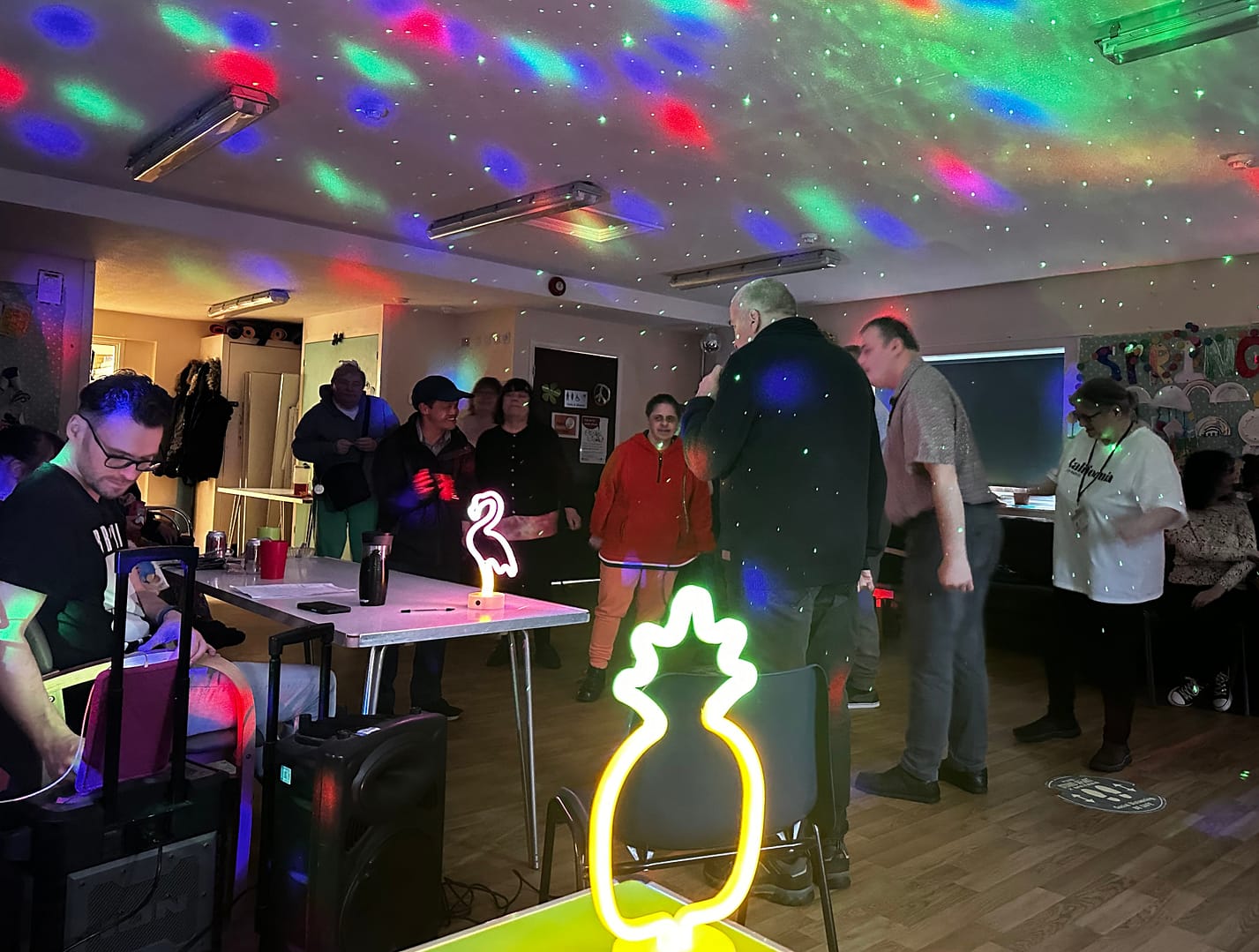 A group of people are dancing as red, green and blue lights shine on the ceiling