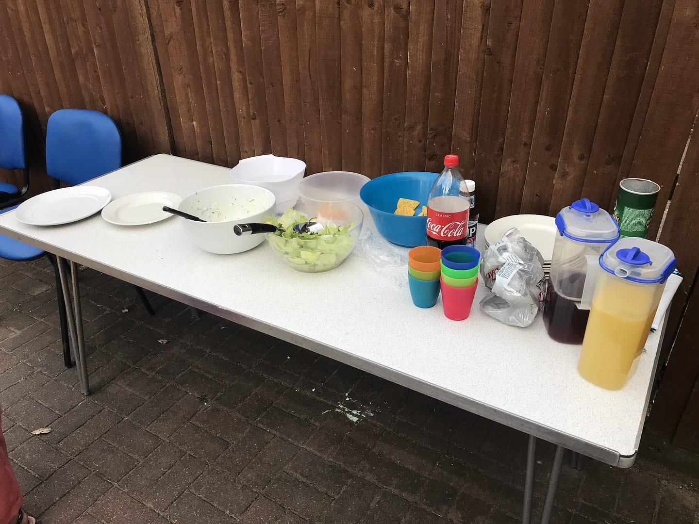 A white table is placed outside and has plates, cups and jugs of squash on it