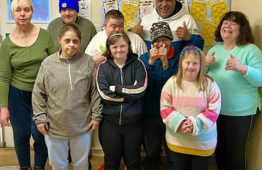 A group of people who attend Reading Mencap's day service are standing and giving a thumbs up gesture