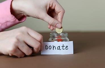a woman's hands can be seen putting a coin into a jar of money