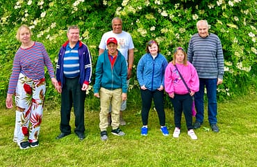 Three women and four men are standing in front of a lush green tree
