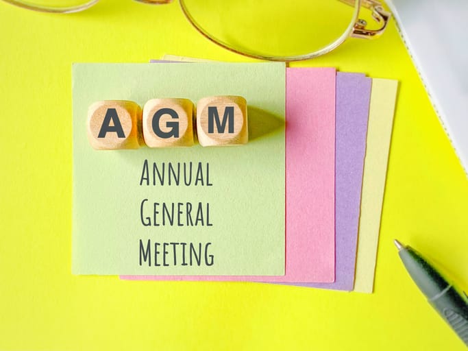 AGM AGM Annual General Meeting text with paper and wooden cubes background.