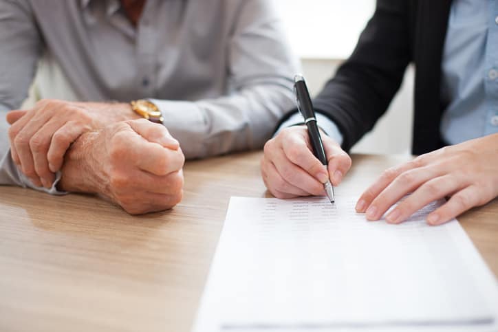 Two people are sitting at a desk. One is holding a pen and is signing a document.